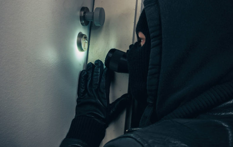 Maskierter Einbrecher mit Taschenlampe an Haustür in der Nacht