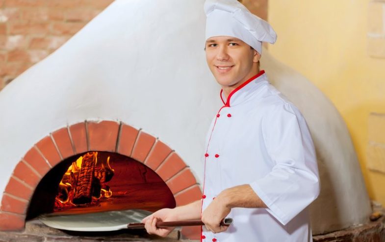 Männlicher Koch schiebt eine Pizza in den Steinofen.