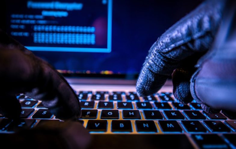 Hacker mit schwarzen Handschuhen bedient einen Laptop.