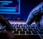 Hacker mit schwarzen Handschuhen bedient einen Laptop.