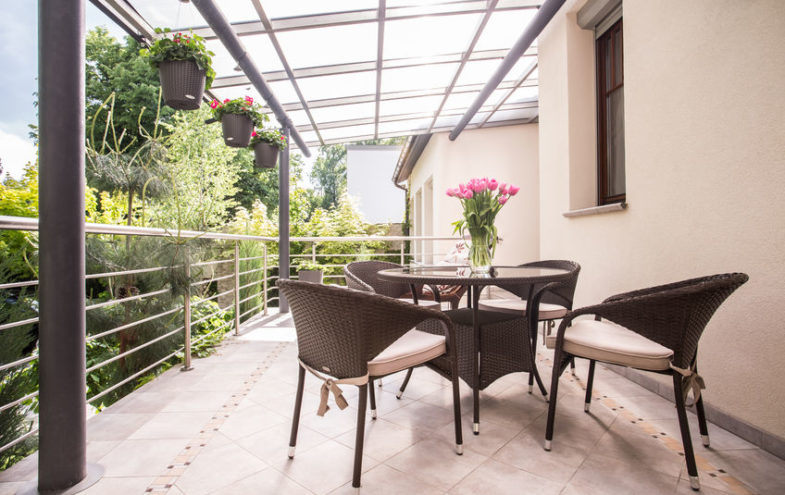 Terrasse mit Glasdach, darunter Tisch und Stühle.