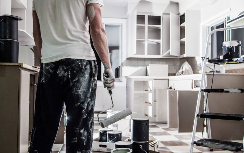 Mann mit Malerausrüstung steht in einer ausgeräumten Küche.