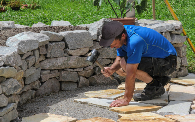 Plattenleger verlegt Natursteinplatten auf einem Gartenweg.