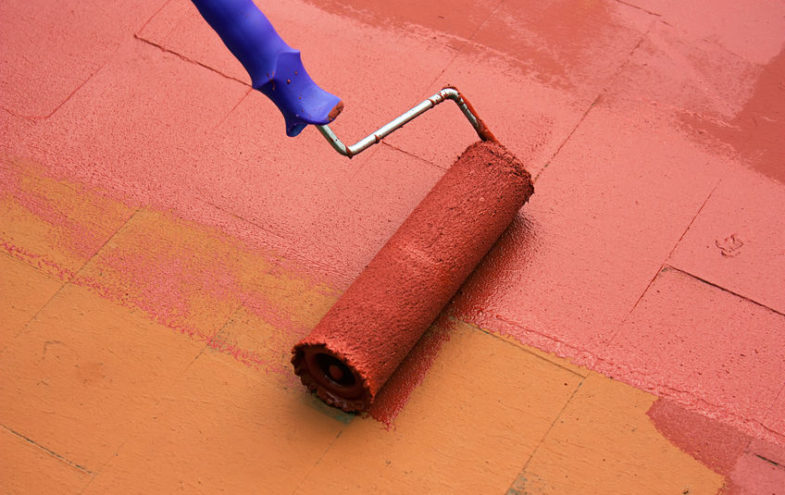 Malerrolle streicht Ziegelplatten mit roter Lackierung.