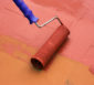 Malerrolle streicht Ziegelplatten mit roter Lackierung.