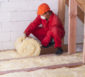 Handwerker verlegt Glaswolldämmung auf dem Dachboden.