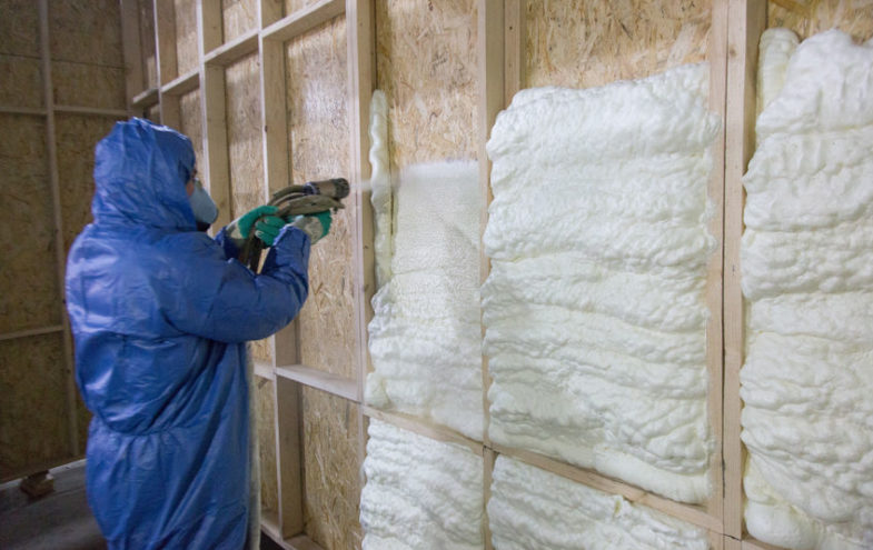 Arbeiter in Schutzkleidung trägt Dämmschaum auf eine Wand auf.