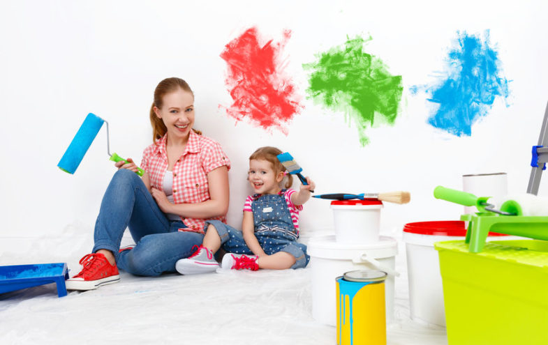 Mutter und Tochter sitzen mit Streichutensilien vor einer weissen Wand mit Farbklecksen.