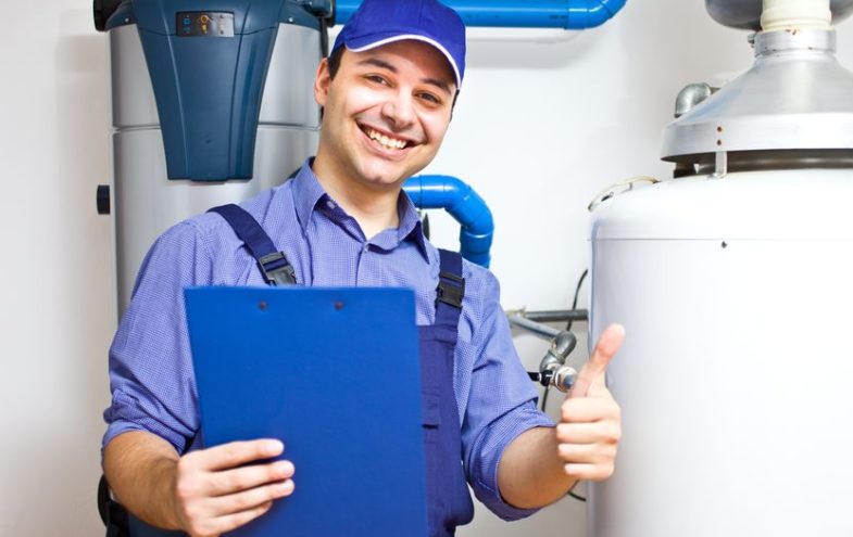 Lächelnder Handwerker mit Checkliste vor einem Warmwasserspeicher.
