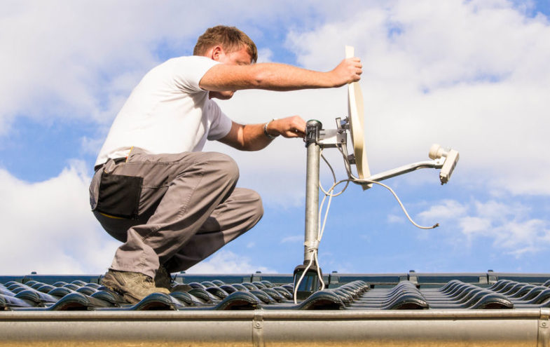Handwerker steht auf einem Dach und richtet eine Satellitenschüssel aus.