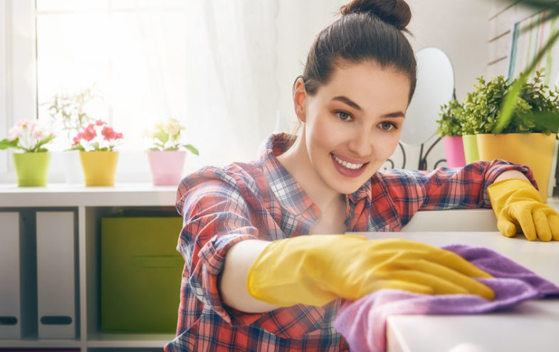 Junge Frau putzt im Haushalt mit Handschuhen und Tuch.