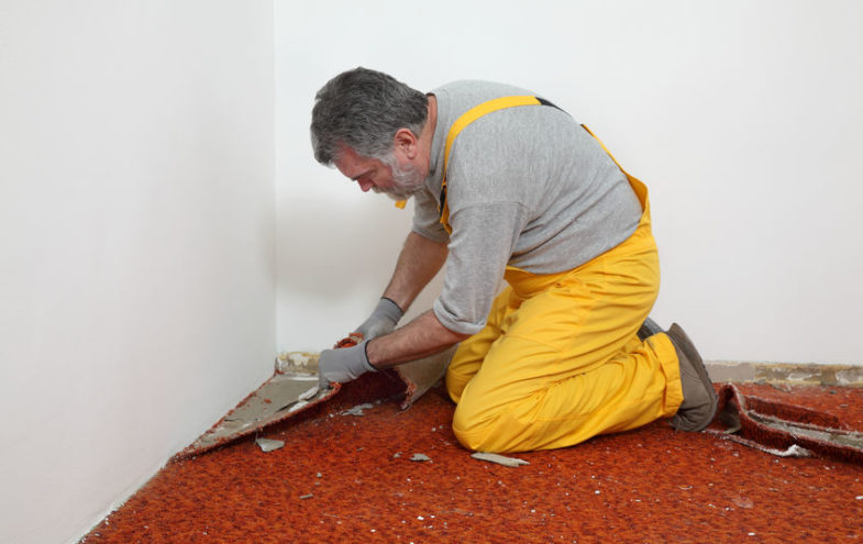 Männlicher Handwerker entfernt einen roten Teppich.