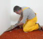 Männlicher Handwerker entfernt einen roten Teppich.