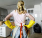 Frau mit Gummihandschuhen steht vor einem zu putzenden Zimmer.