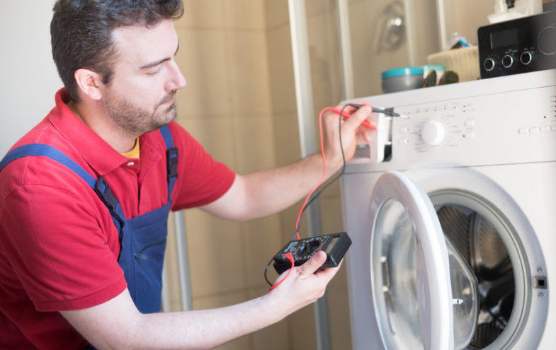 Männlicher Handwerker überprüft die Elektronik einer Waschmaschine.