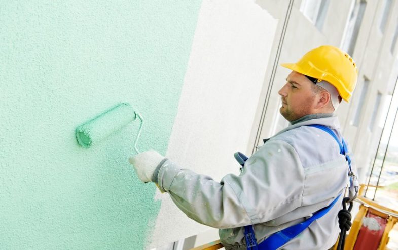 Maler mit Farbrolle streicht die Fassade eines Hauses in Minzgrün.