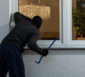 Einbrecher mit Skimaske und Brecheisen blickt durch ein Fenster ins Haus.