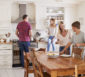 Vierköpfige Familie kocht und lacht gemeinsam in einer modernen, hellen Küche.