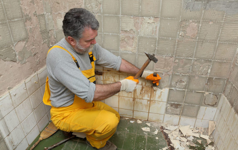 Handwerker meisselt alte Fliesen von einer Badezimmerwand.