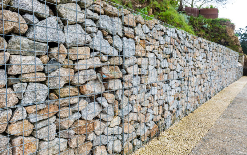 Gabione aus Draht und Natursteinen als Stützmauer entlang eines Gehweges.