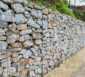 Gabione aus Draht und Natursteinen als Stützmauer entlang eines Gehweges.