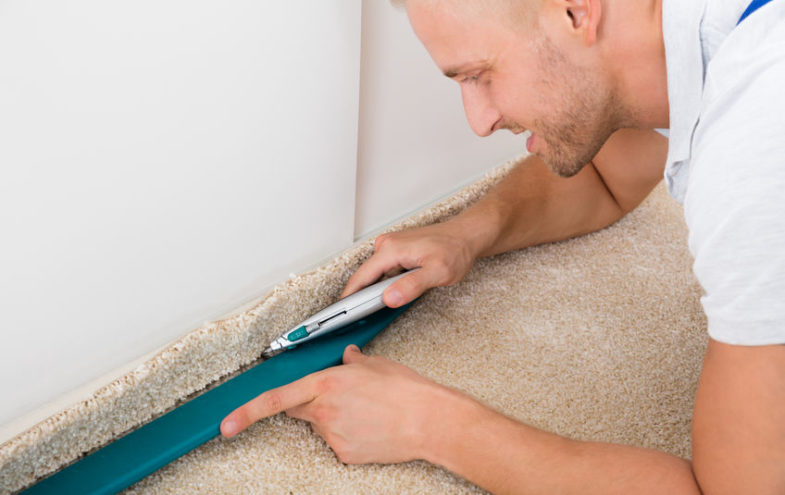 Handwerker mit Teppichmesser trimmt den Rand eines beigen Teppichs.