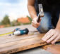 Handwerker mit Hammer befestigt Holzdielen als Terrassenbelag.