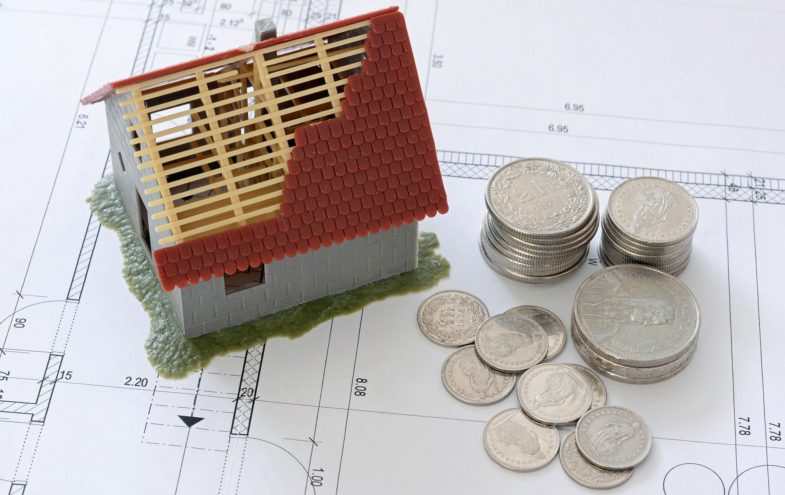 Ein Modellhaus und Geldmünzen auf einem Hausbauplan.