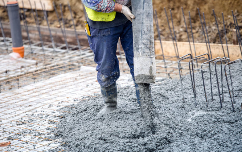 Arbeiter mit Schlauch giesst ein Fundament aus Beton.
