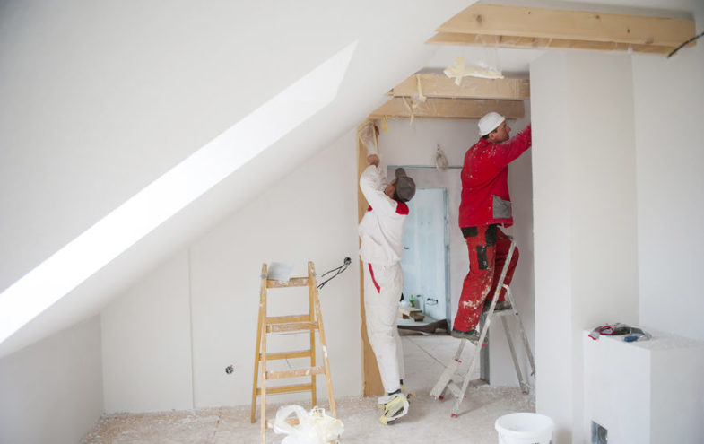Zwei Handwerker führen Maler- und Gipserarbeiten in einem Dachzimmer aus.