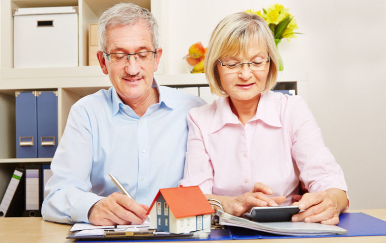 Älteres Paar kalkuliert gemeinsam die Nebenkosten mit Dokumenten und Taschenrechner.