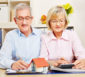 Älteres Paar kalkuliert gemeinsam die Nebenkosten mit Dokumenten und Taschenrechner.