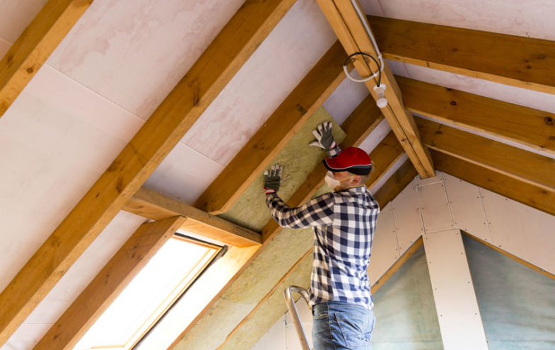 Handwerker auf einer Leiter im Dachboden installiert Dämmwolle beim Estrich-Ausbau.