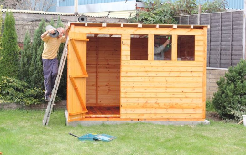 Zwei Handwerker bauen ein kleines Gartenhaus aus Holz zusammen.