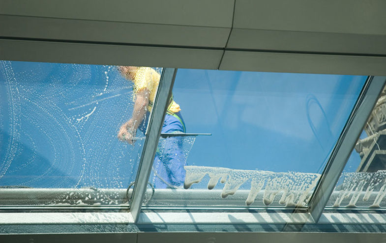Reinigungskraft auf einem Glasdach reinigt die Glasscheiben.
