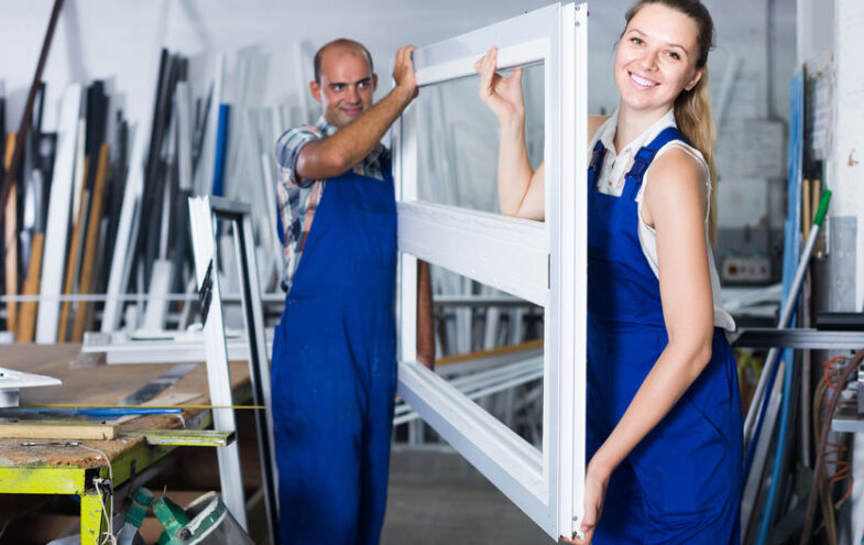 Zwei Handwerker in einer Werkstatt tragen einen Fensterrahmen.