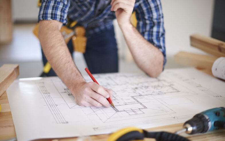 Bauleiter auf einer Baustelle arbeitet mit Bleistift an einer Bauskizze.