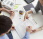 Junges Paar am Bürotisch mit einer Architektin unterschreibt einen Architektenvertrag.