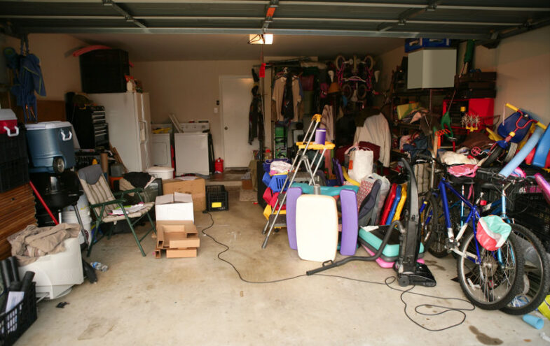 Chaotische Garage vollgepackt mit Gartenutensilien, Möbeln, Fahrrädern und mehr.