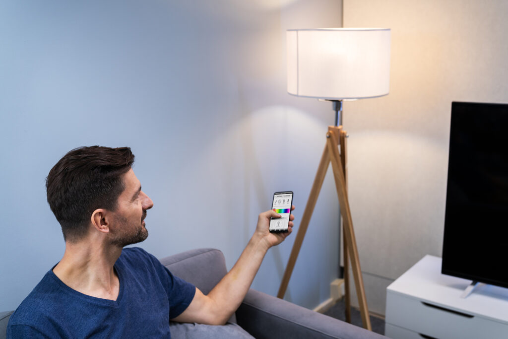 Mann bedient per Smartphone eine Lampe im Wohnzimmer.