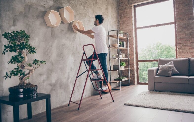 Mann auf einer Leiter hängt Wanddekoration aus Holz auf.